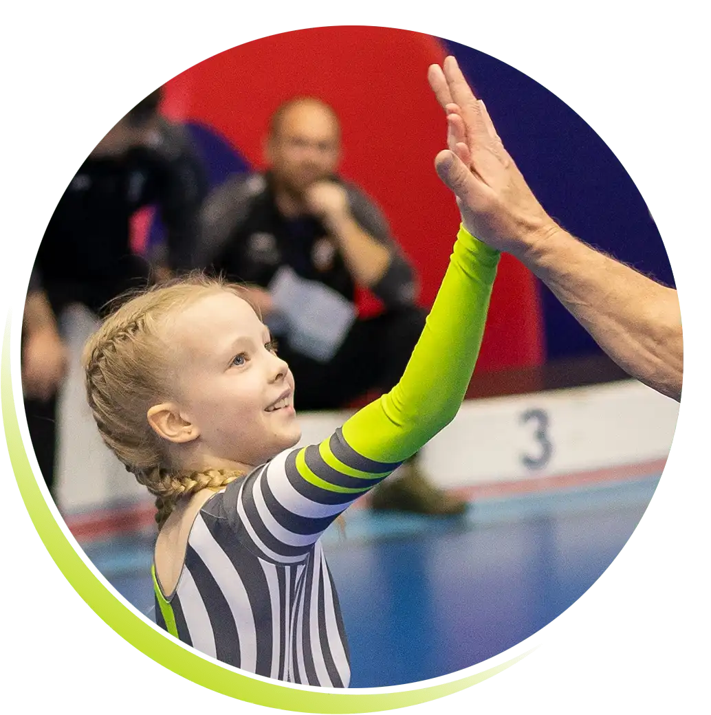 Mała dziewczynka w klubowym stroju odważnie i z radością "przybija piątkę" trenerowi. W tle podium.