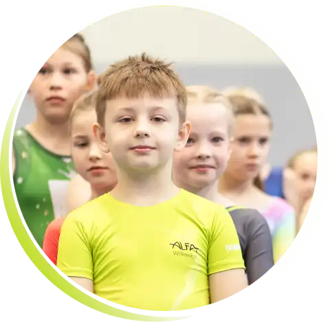 Dumny i pewny siebie chłopczyk w koszulce UKS Alfa Wilkowice stoi wyprostowany na tle grupki innych dzieci.